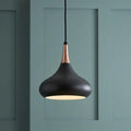 Matte black and copper teardrop pendant light hanging against a green paneled wall.