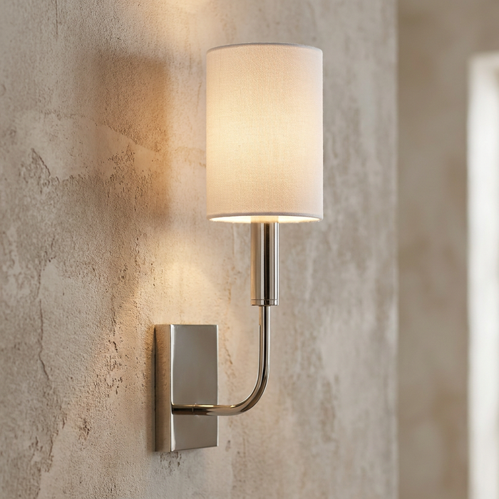 Feiss Brianna 1 light polished nickel wall light with a white cylindrical fabric shade on a textured wall.