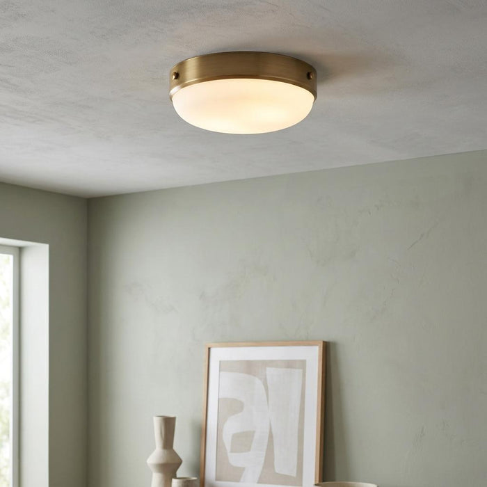 Feiss Cadence antique brass flush ceiling light with an opal glass dome against a light green wall.