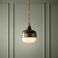 Feiss Cadence mini pendant light with black and brass metalwork and opal glass, hanging against a green paneled wall.