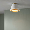 Matte white flush ceiling light with gold interior and vertical slits casting sunburst shadows.