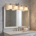 Feiss Concord 4-light bathroom wall fixture with white shades mounted above a mirror in a marble bathroom.