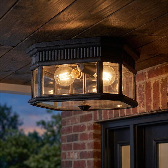 Black hexagonal outdoor flush mount ceiling light with glass panels and glowing bulbs on a wooden porch ceiling.