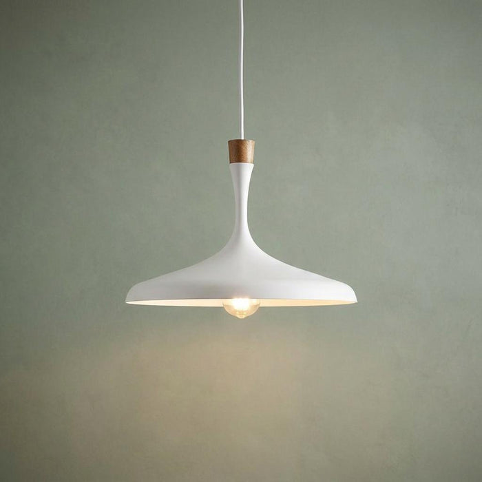 A matte white pendant light with a wood accent and warm bulb, hanging against a muted green wall.