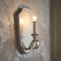 Sunrise silver candle-style wall light with a glowing bulb mounted on a rustic, textured plaster wall.