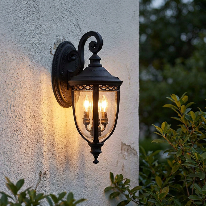 Traditional black lantern wall light with seeded glass and glowing bulbs, mounted on a white stucco wall.