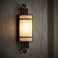 Grecian bronze wall light with geometric cage and glowing frosted shade mounted on a textured dark wall.