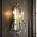 Feiss Gianna 3-light gilded silver wall sconce with crystal accents and mirrored backplate on a dark wood wall.