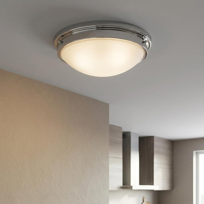 Polished chrome flush mount ceiling light with a frosted glass dome, glowing in a modern kitchen.