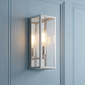 Polished nickel wall light with seeded glass panels mounted on a light blue paneled wall.