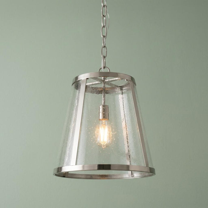 Tapered seeded glass lantern with a polished nickel frame hanging against a soft green wall.