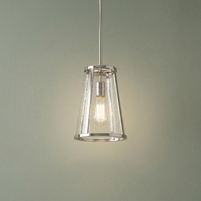 Polished nickel lantern pendant with seeded glass and a lit Edison bulb against a sage green wall.