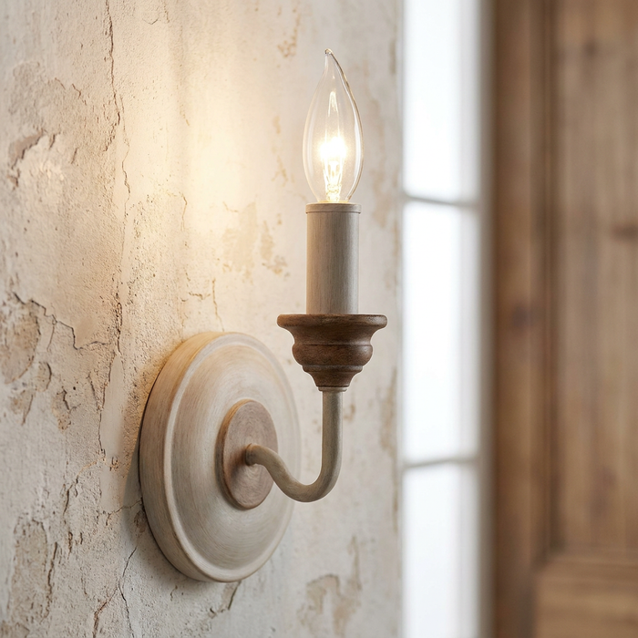 Chalk-washed wooden wall sconce with a glowing candle bulb on a rustic textured wall.
