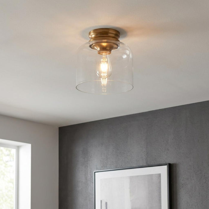 Feiss Hounslow brass flush mount light with a clear glass bell shade on a white ceiling.