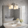 Two-light polished chrome vanity light with frosted shades above a mirror in a marble-tiled bathroom.