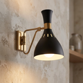 Feiss Joan matte black and brass wall sconce with hourglass shade mounted on a textured plaster wall.