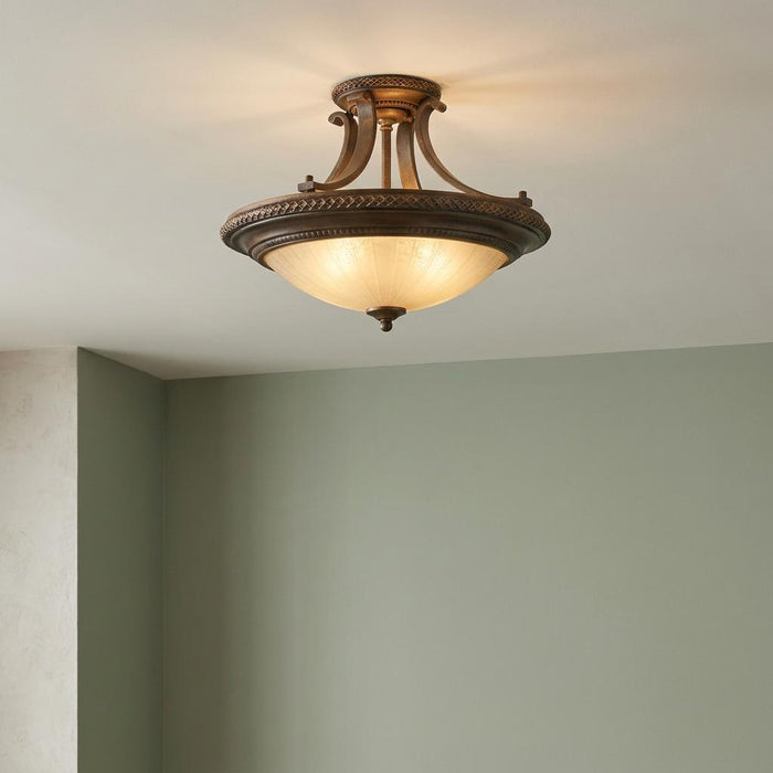 Ornate gold and bronze semi-flush ceiling light with a scavo glass bowl shade mounted in a room with green walls.