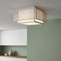 Square flush mount ceiling light with a silver geometric lattice frame and white diffuser against a green wall.