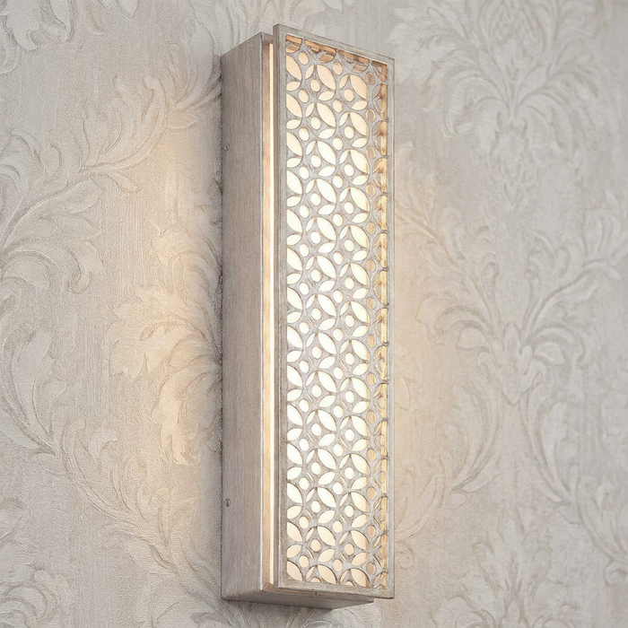 Rectangular silver wall light with a decorative lattice pattern glowing against damask-patterned wallpaper.
