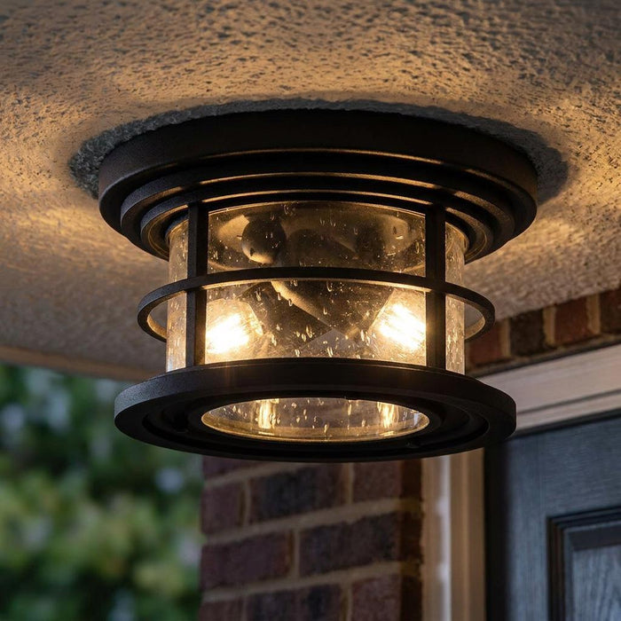Industrial black metal flush mount porch light with seeded glass and glowing bulbs mounted on a white textured ceiling.