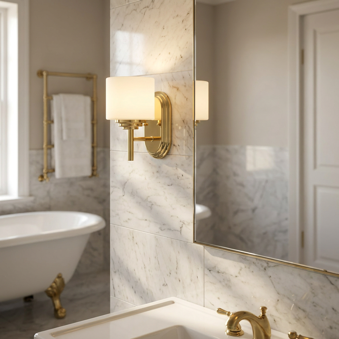 Polished brass wall light with an opal glass shade mounted on a marble wall in a luxurious bathroom.