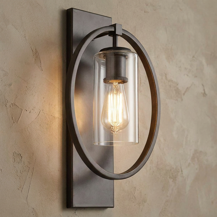 Feiss Marlena wall light with a circular bronze frame and a clear glass cylinder shade holding a glowing Edison bulb.