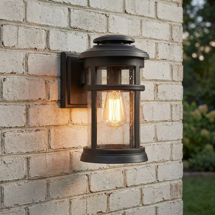 A bronze outdoor wall light with seeded glass and a warm Edison bulb mounted on a white brick wall.