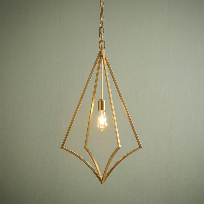 Geometric brass diamond-shaped pendant light with an exposed glowing bulb against a sage green wall.