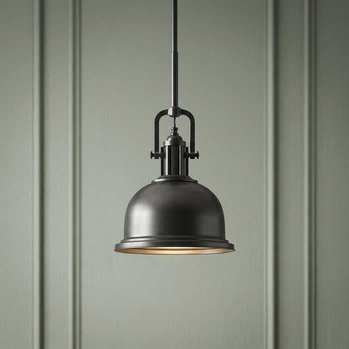 Industrial bronze pendant light with a dome shade hanging against a sage green paneled wall.