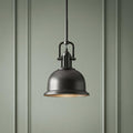 Industrial bronze pendant light with a dome shade hanging against a sage green paneled wall.