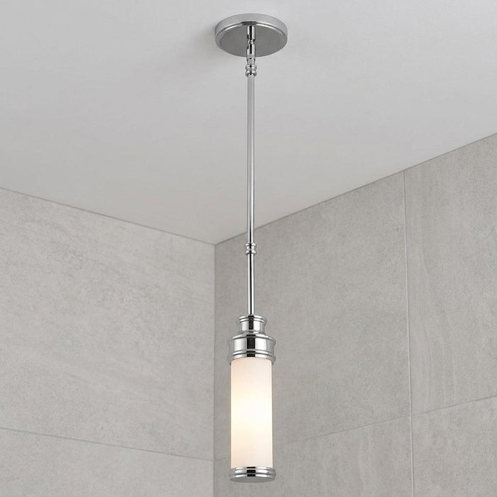 Chrome mini pendant light with a white cylindrical glass shade hanging against a grey tiled bathroom wall.