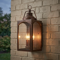 A Feiss Randhurst copper outdoor wall lantern with seeded glass and three lights mounted on a brick wall.