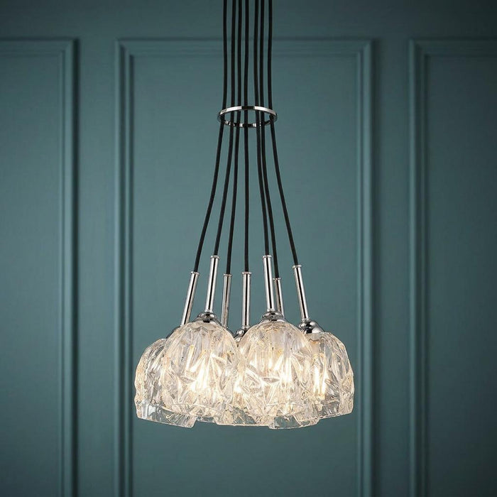 Feiss Rubin 7-light chandelier with textured glass shades and polished nickel accents against a teal paneled wall.