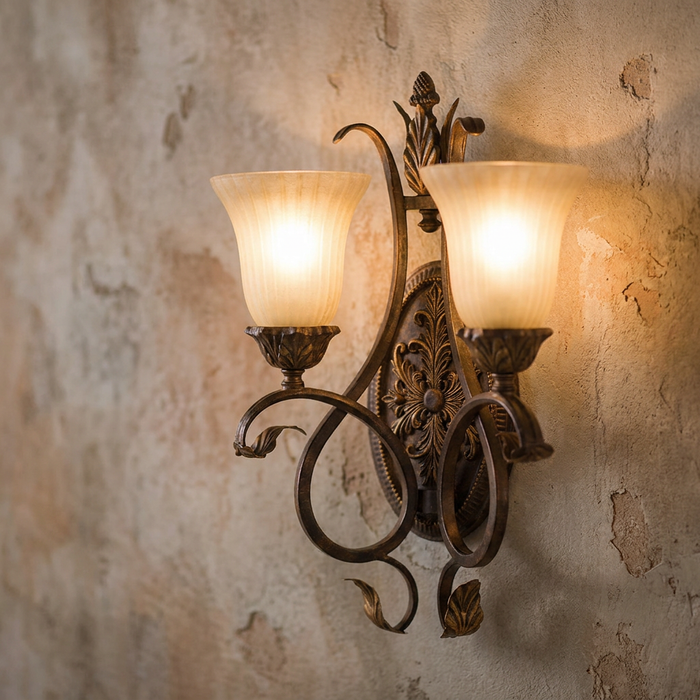 Ornate twin-arm wall sconce with amber glass shades glowing against a rustic, textured plaster wall.