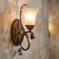 Feiss Sonoma Valley wall sconce with ornate bronze scrollwork and cream glass shade on a rustic plaster wall.
