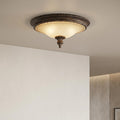 Bronze Art Deco flush ceiling light with a warm frosted glass shade and decorative finial on a white ceiling.