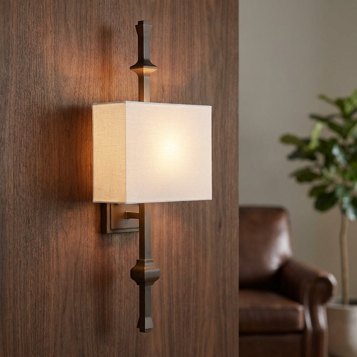 Antique bronze wall light with a rectangular linen shade glowing on a dark wood-paneled wall.