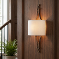 Gold leaf wall sconce with a white fabric shade, mounted on dark wood paneling.