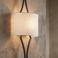 Feiss Tilling wall light with a weathered iron frame and cream linen shade on a rustic textured wall.