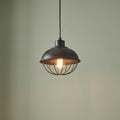 Industrial antique iron pendant light with a wire cage and Edison bulb, hanging against a sage green wall.