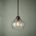 Feiss Urban Renewal mini pendant with a rustic iron finish and seeded glass shade against a sage green background.