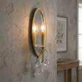 Feiss Valentina wall light with an oval mirrored backplate and hanging crystal droplets on a textured stone wall.