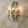 Three-light bronze wall sconce with an oval mirrored backplate and crystal accents on a textured wall.