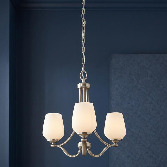 Feiss Vintner 3-light satin nickel chandelier with opal glass shades hanging against a dark blue wall.