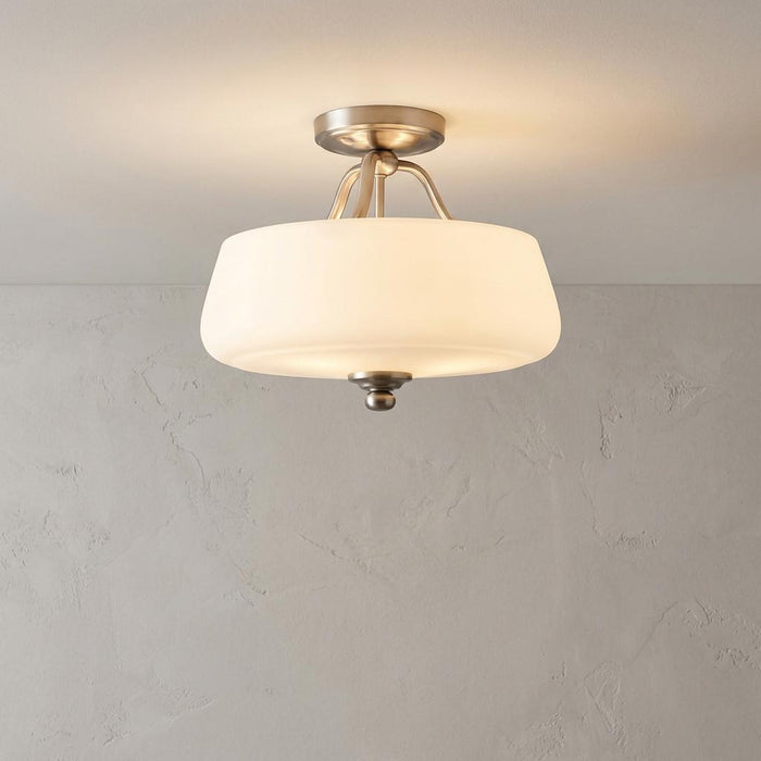 Semi-flush satin nickel ceiling light with a white glass drum shade illuminated against a textured wall.