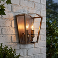 Two-light aged brass wall lantern with glowing candle bulbs mounted on a white brick wall.