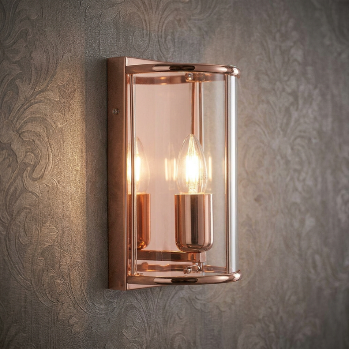Fern Copper single light wall light with glass shade and glowing bulb on grey patterned wallpaper.