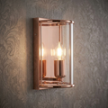 Fern Copper single light wall light with glass shade and glowing bulb on grey patterned wallpaper.