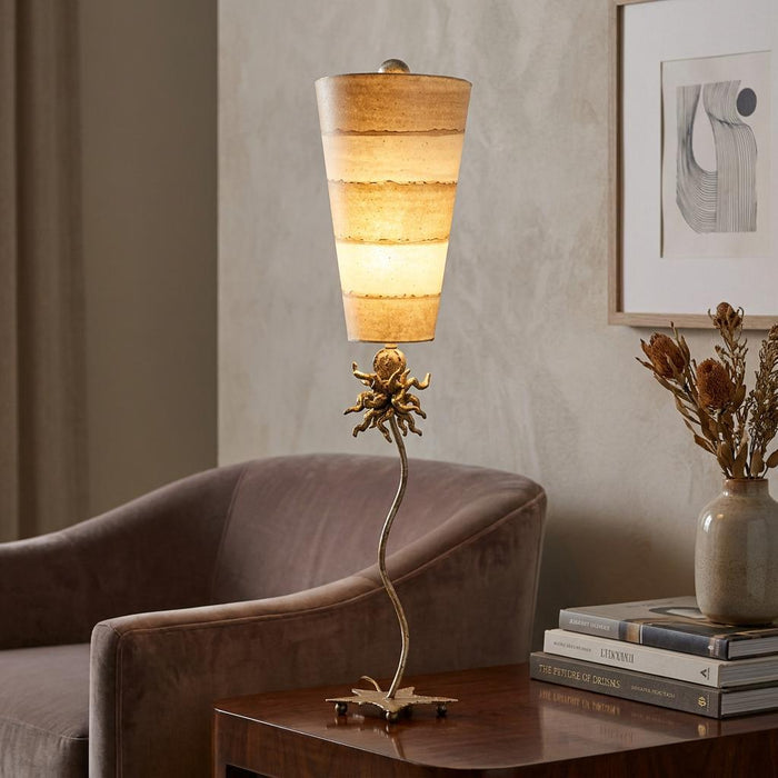 Gold anemone table lamp with a sinuous stem and striped shade glowing on a dark wooden side table.