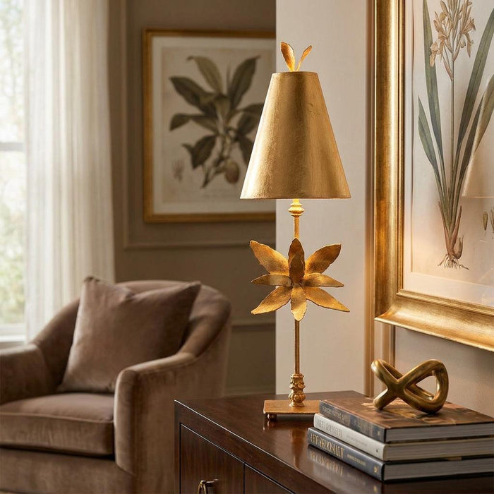 Gold leaf table lamp with a floral leaf motif on its stem, resting on a sideboard in a warm living room.